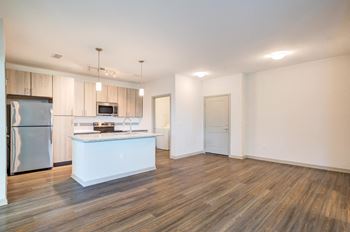 An empty living room with a kitchen with stainless steel appliances